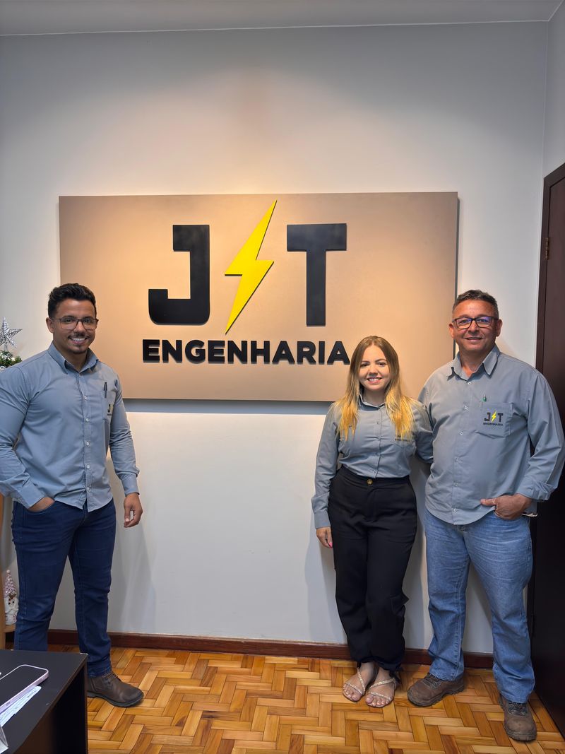 Sócios e equipe da JT Engenharia em frente ao logo da empresa